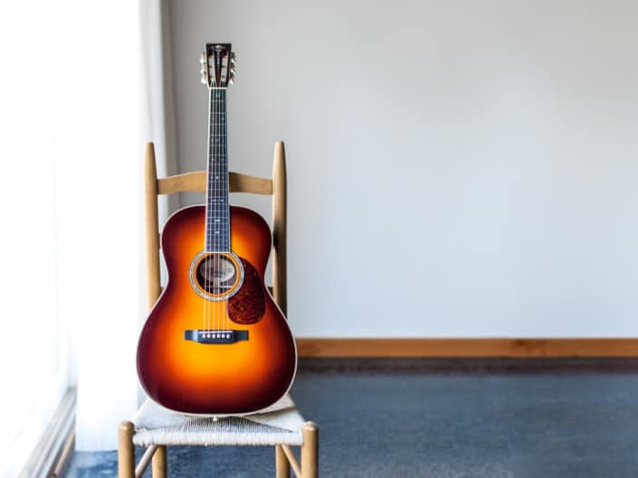 12 Fret 000 acoustic guitar handcrafted from Adirondack Spruce and Brazilian Rosewood. On a chair